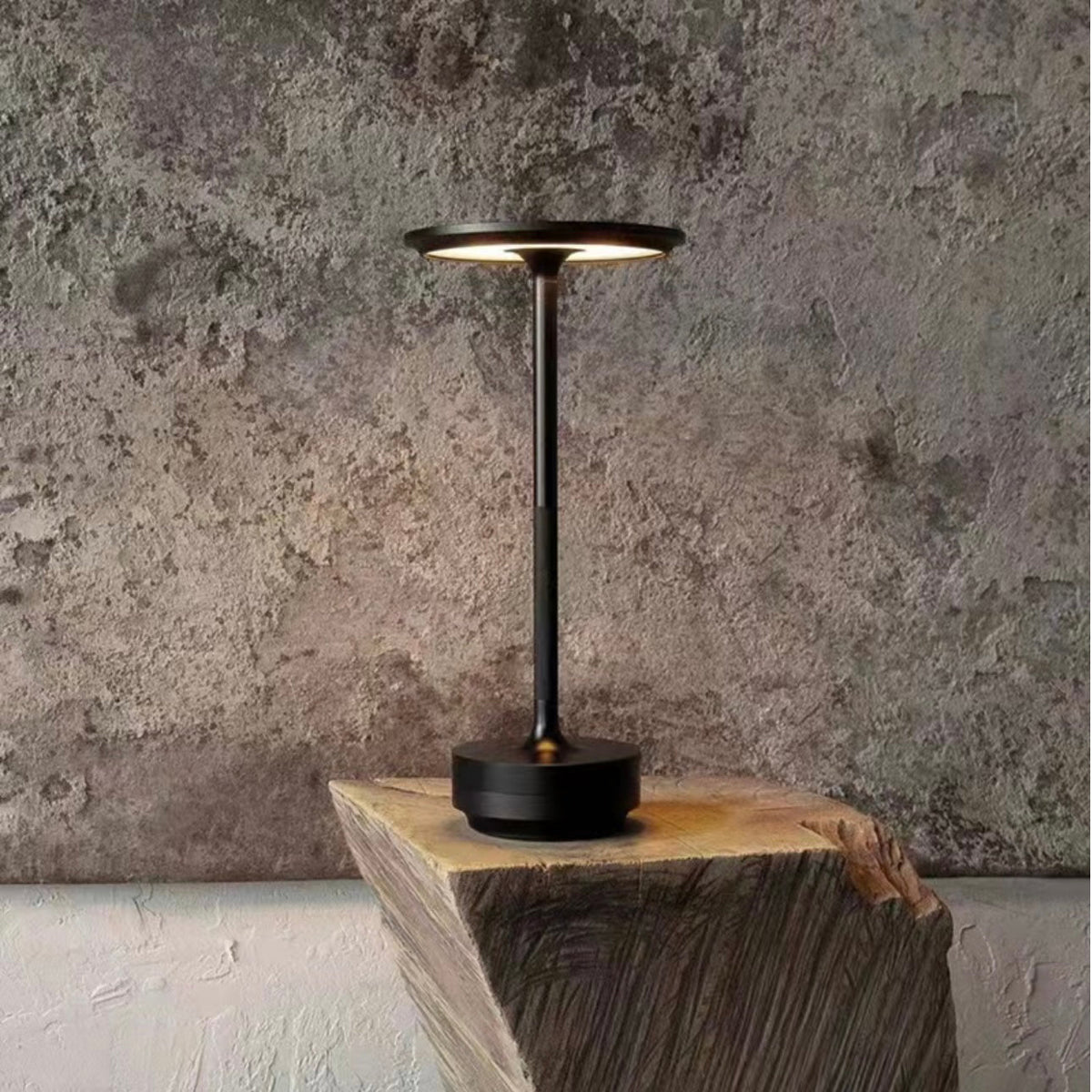 Dark rechargeable table lamp on wooden stump with warm glowing top