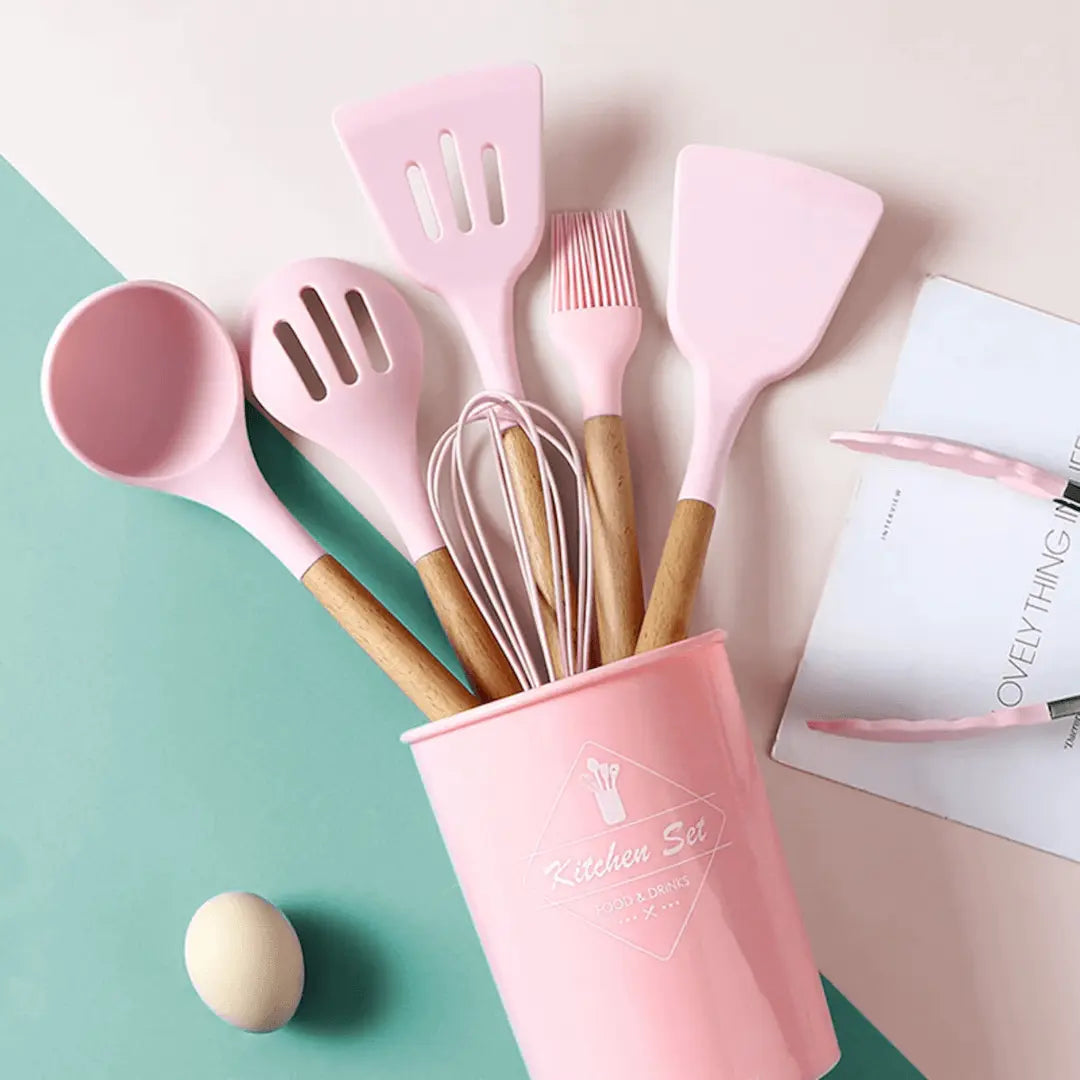 Pastel silicone utensil set with wooden handles in a pink holder cup, spatulas and whisk