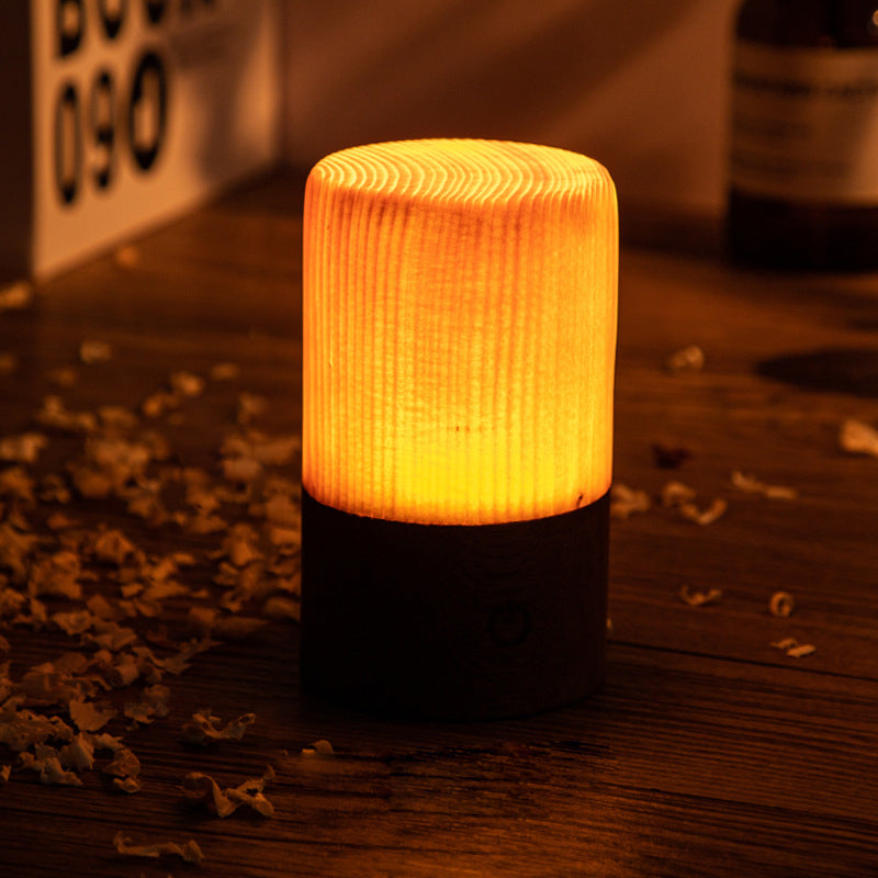 Cylindrical woodgrain LED night light on dark base with warm amber glow