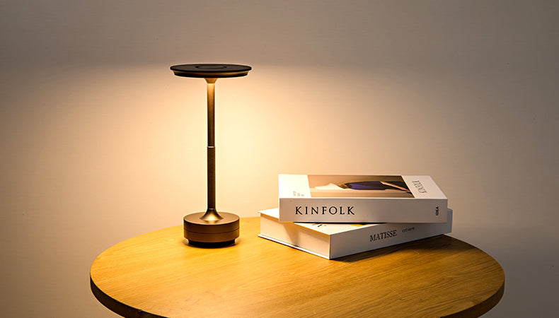 Cordless LED table lamp with bronze frame and warm lit round top on a wooden table