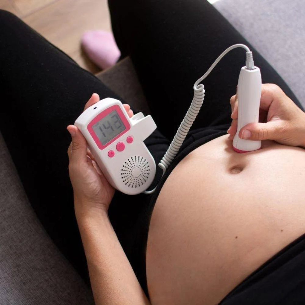 Fetal Doppler probe held against belly with coiled cable and LCD monitor