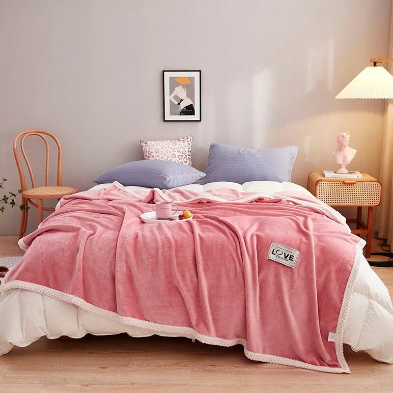 Pink fleece throw blanket draped over bed with white trim and LOVE heart tag