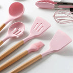 Pink silicone cooking utensils with wooden handles, including slotted spatula and whisk