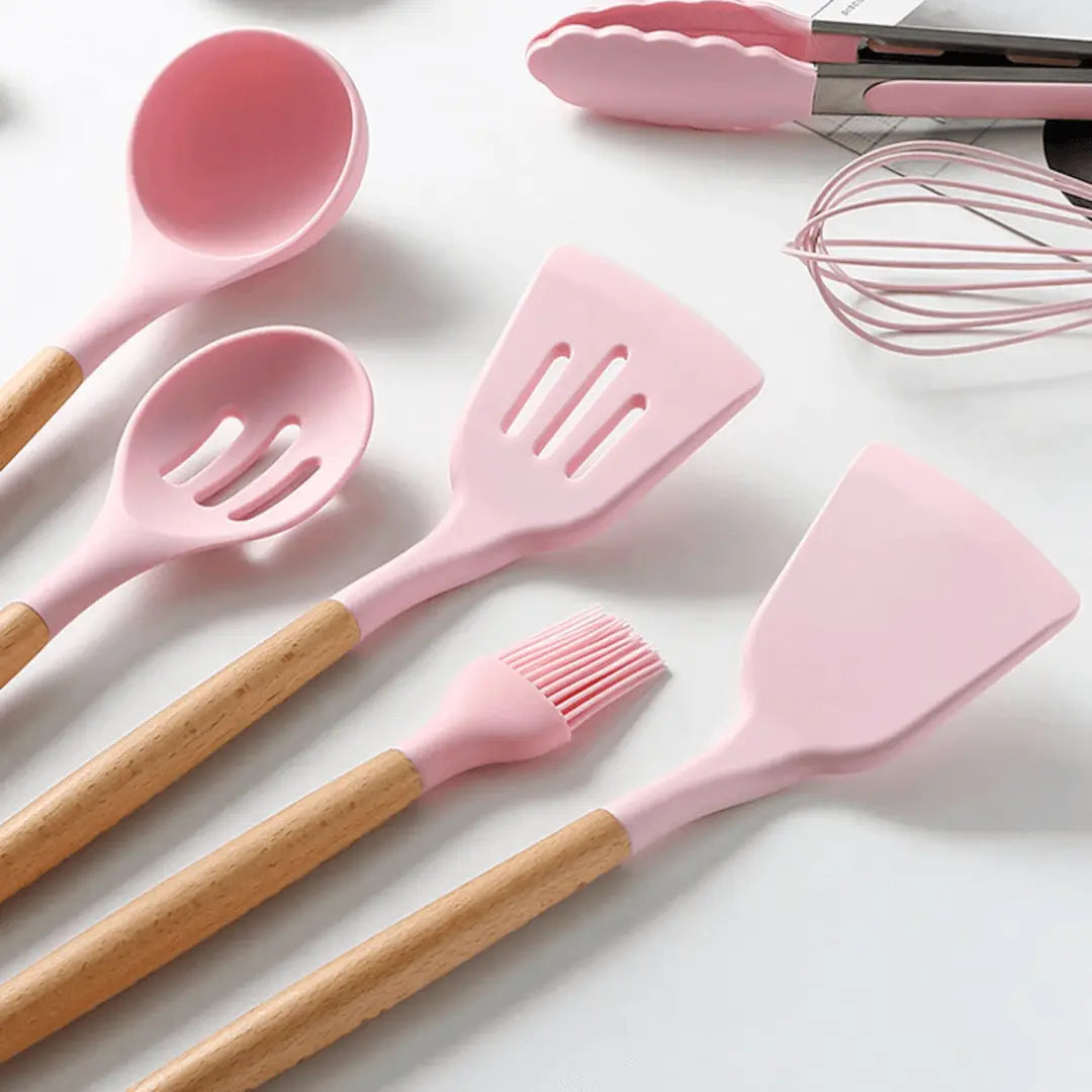 Pink silicone cooking utensils with wooden handles, including slotted spatula and whisk