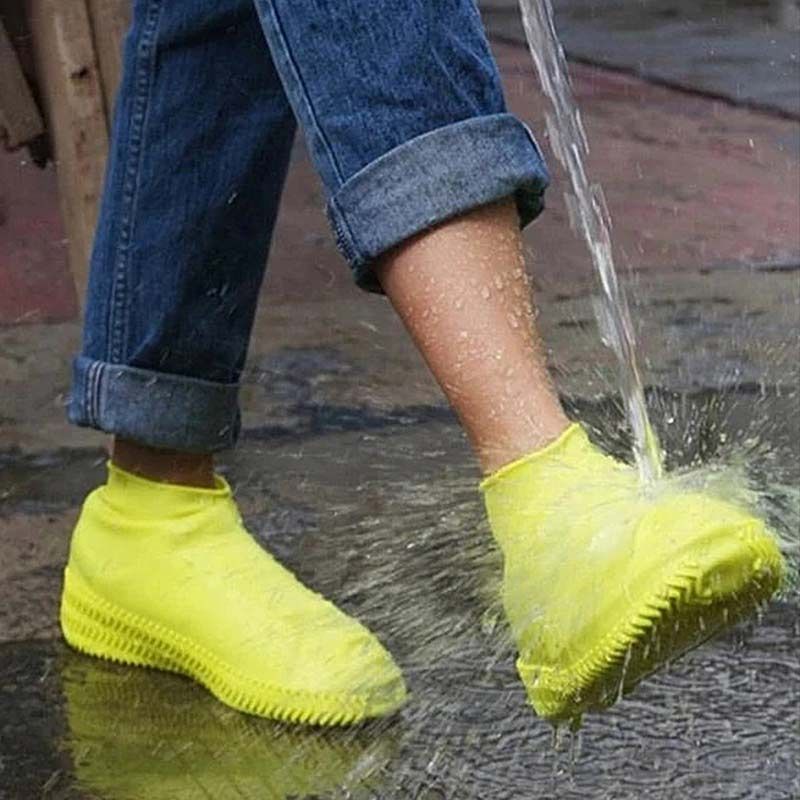 Yellow waterproof elastic shoe covers on feet with textured zigzag tread sole