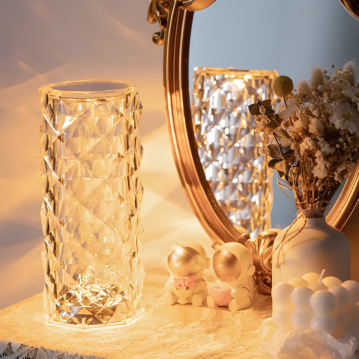 Faceted crystal table lamp glowing warm amber, cylindrical crystal shade on a surface.