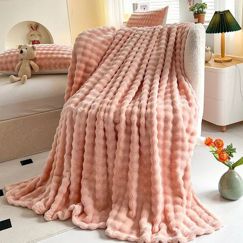 Bubble-texture fleece blanket in light coral pink with ridged bubble texture, folded on couch