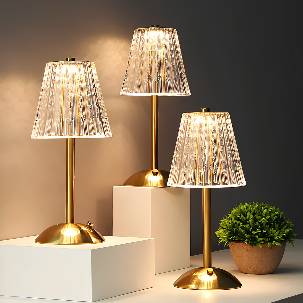 Set of gold table lamps with clear pleated crystal shades and round bases, lit.