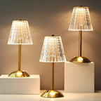 Three gold table lamps with clear pleated crystal shades and round bases, lit.