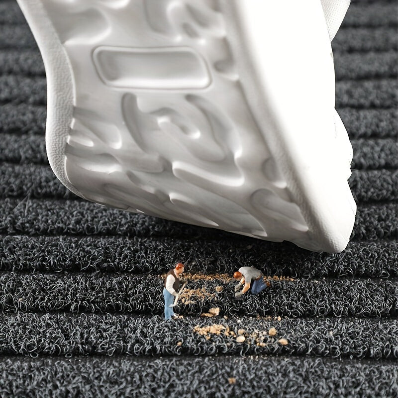 Black doormat with grippy textured surface under a shoe, with small debris