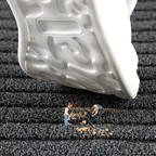 Black doormat with grippy textured surface under a shoe, with small debris