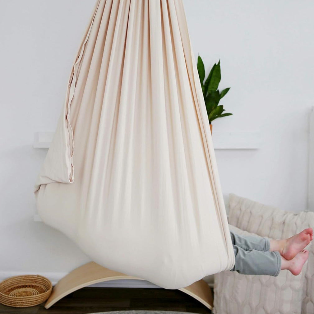 Beige kids' cotton hammock swing cocoon suspended, child lying with legs outside.