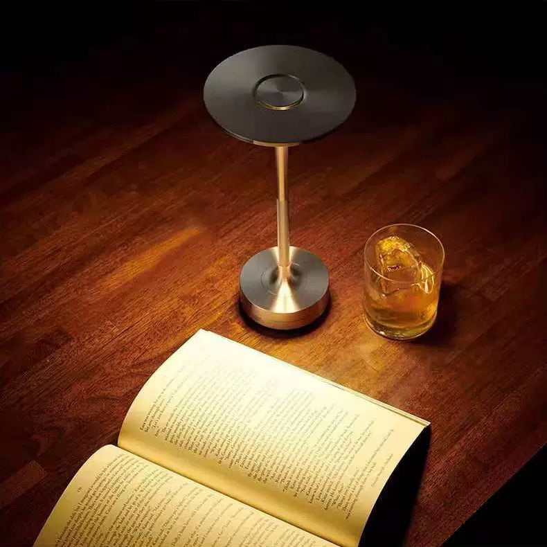 Cordless LED table lamp with bronze finish, circular base, and warm lit round top