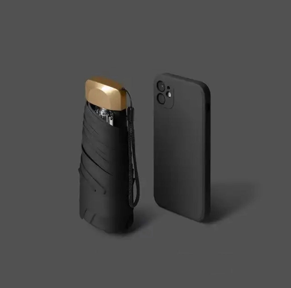 Black mini travel umbrella, folded pocket size with carry strap and gold cap.