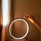 Minimalist round LED table lamp with touch control, hand reaching toward glowing halo ring