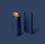 Dark blue mini travel umbrella, folded pocket size with carry strap and gold cap.