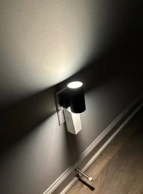 Black plug-in LED wall light with two-prong plug and warm illuminated top ring
