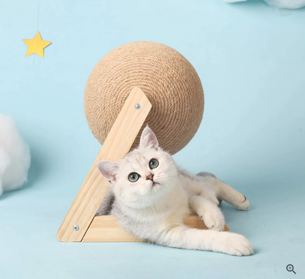 Cat scratching toy with tan sisal ball on wooden stand, with a white cat crouching.