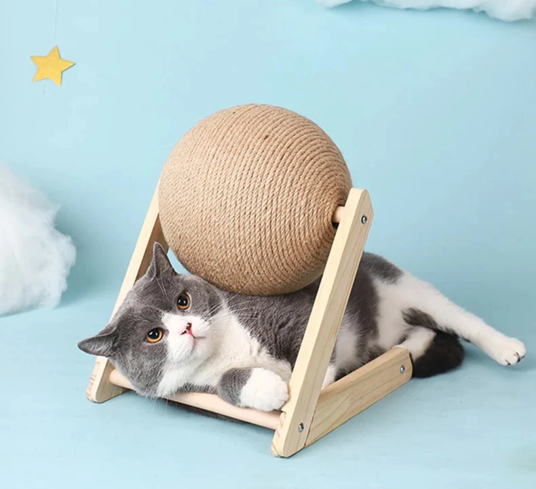 Cat scratching toy with tan sisal ball on wooden stand, with a gray cat resting and pawing.