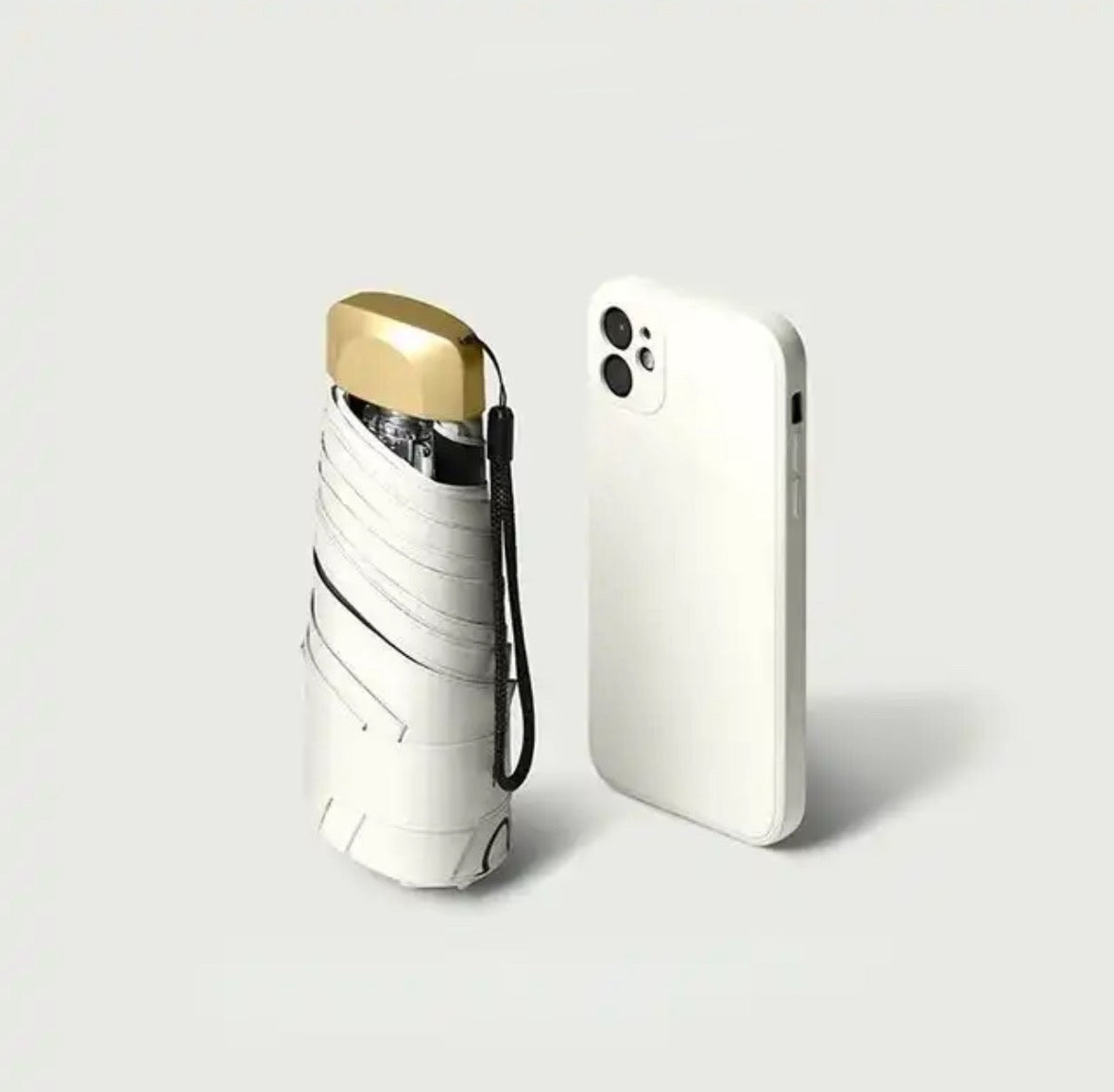 White mini travel umbrella, folded pocket size with carry strap and gold cap.