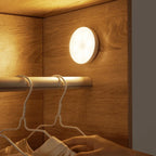 Round warm-white LED motion sensor light mounted on closet wall, glowing