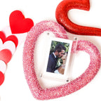 White digital photo frame with photo display inside a red glitter heart decoration.