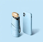 Light blue mini travel umbrella, folded pocket size with carry strap and gold cap.