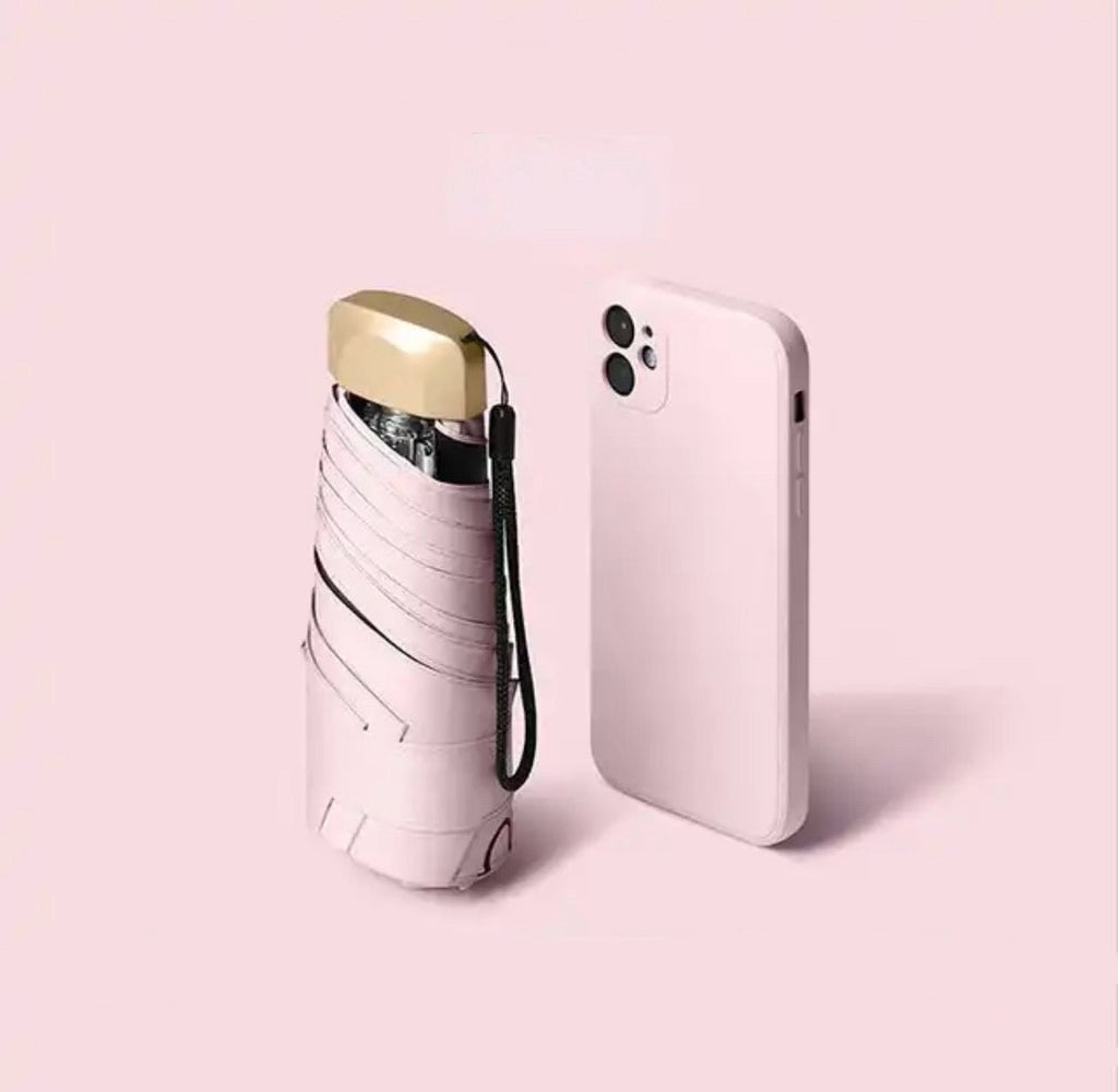 Pink mini travel umbrella, folded pocket size with carry strap and gold cap.