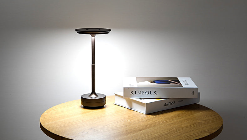 Rechargeable table lamp with warm glowing top and dark base on wooden surface