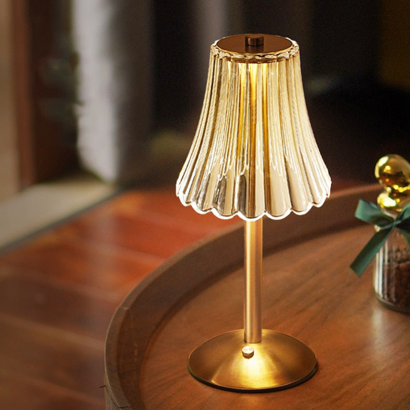 Golden table lamp with pleated crystal shade and round brushed-metal base, lit.
