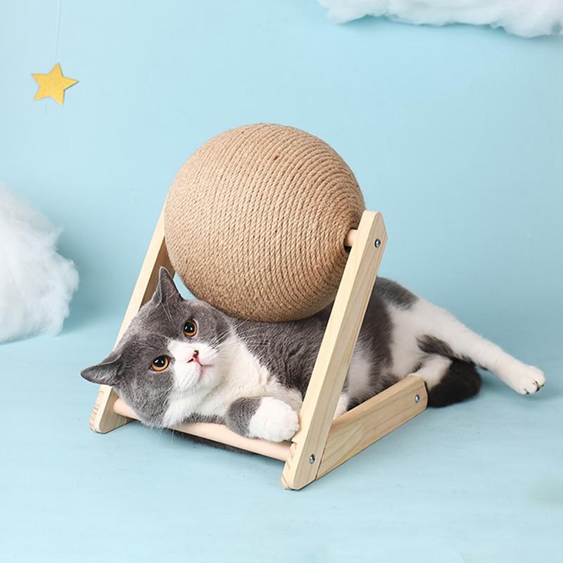 Cat scratching toy with tan sisal ball on wooden stand, with a gray and white cat lying inside.