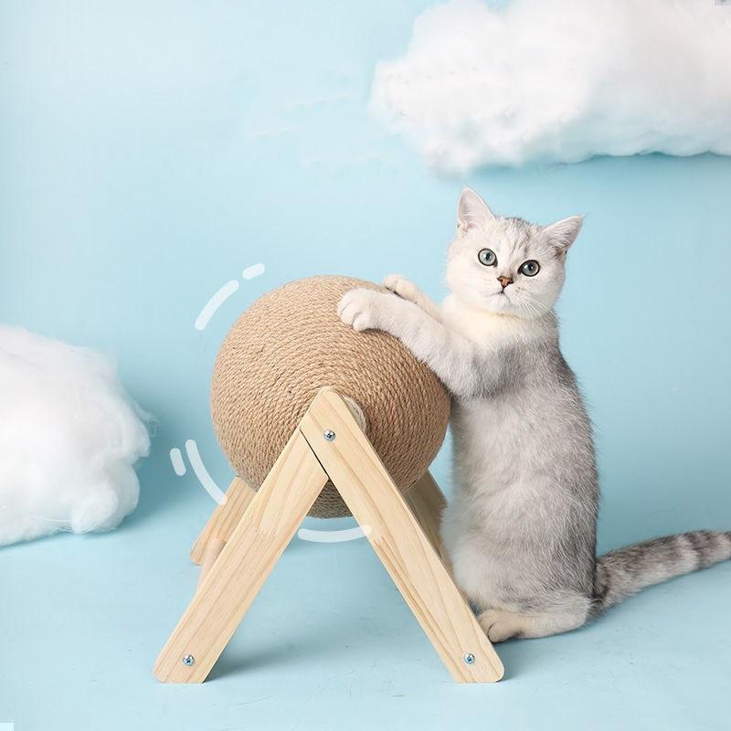 Cat scratching toy with tan sisal ball on wooden stand, with a white cat sitting by it.