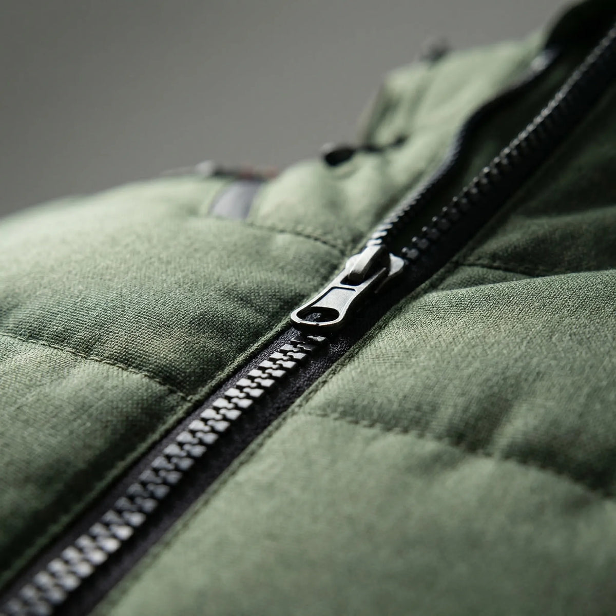 Insulated ski jacket close-up: black zipper and quilted green padded fabric.