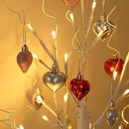 Lit birch tree branch with red and silver heart ornaments hanging on wires