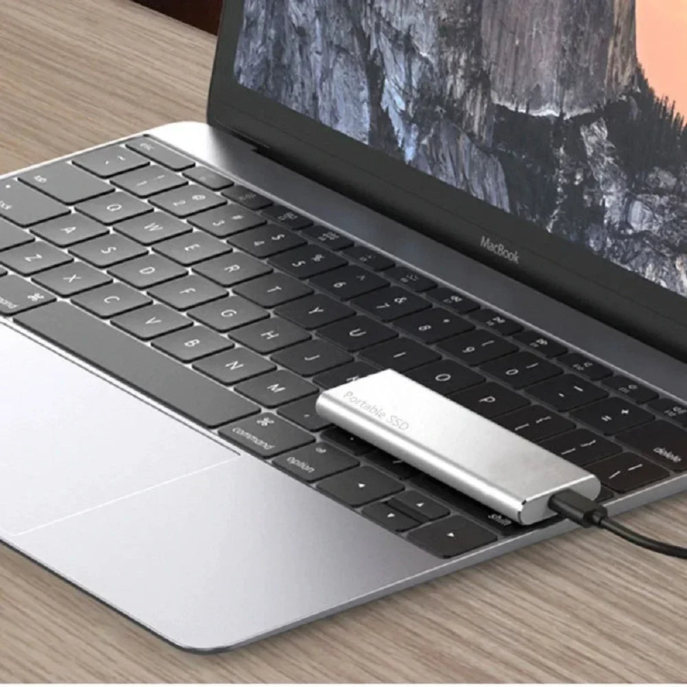 Silver portable external SSD plugged into a laptop with USB cable.