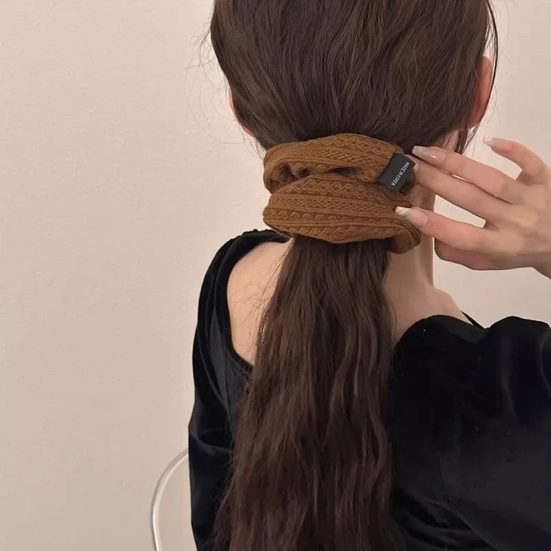 Brown knit hair scrunchie on a ponytail, patterned fabric with small label tag.