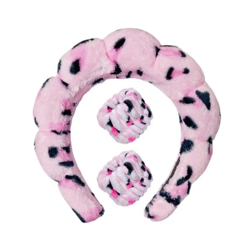 Pink plush spa headband with matching wrist towels and black paw-dot accents.