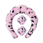 Pink plush spa headband with matching wrist towels and black paw-dot accents.