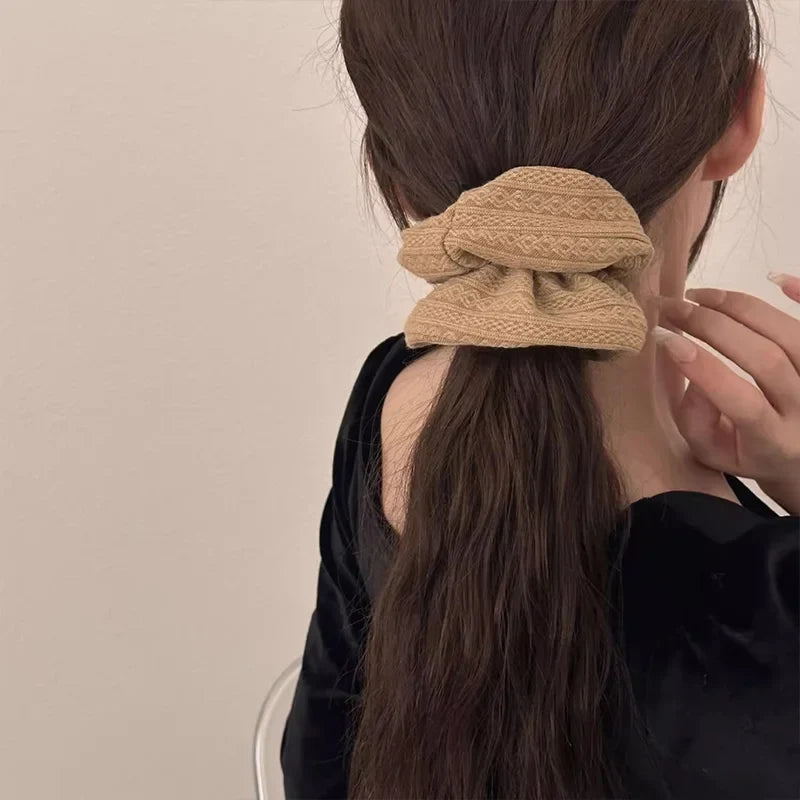 Beige knit hair scrunchie worn in a ponytail, with ruffled stitched texture.
