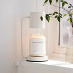 White electric candle warmer lamp with glass jar candle on round base, open-top shade