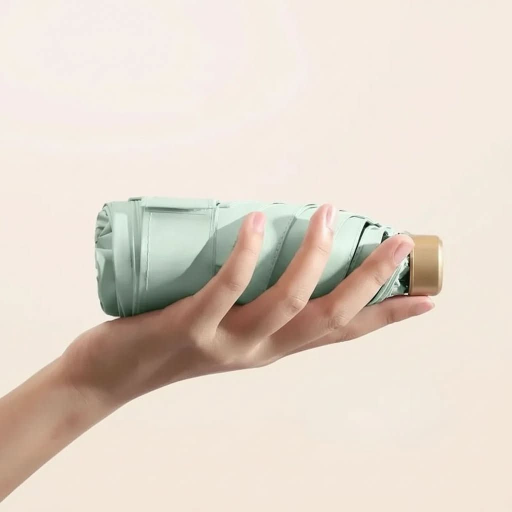 Compact travel umbrella, folded mint green with hand holding the protective cover