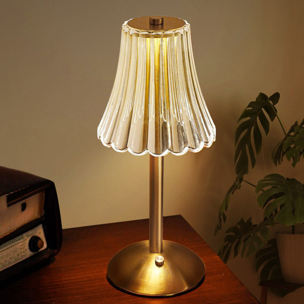 Gold table lamp with clear ribbed crystal shade and round base, warm light on.