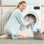 Woman loading a washing machine with laundry, smiling at the camera.