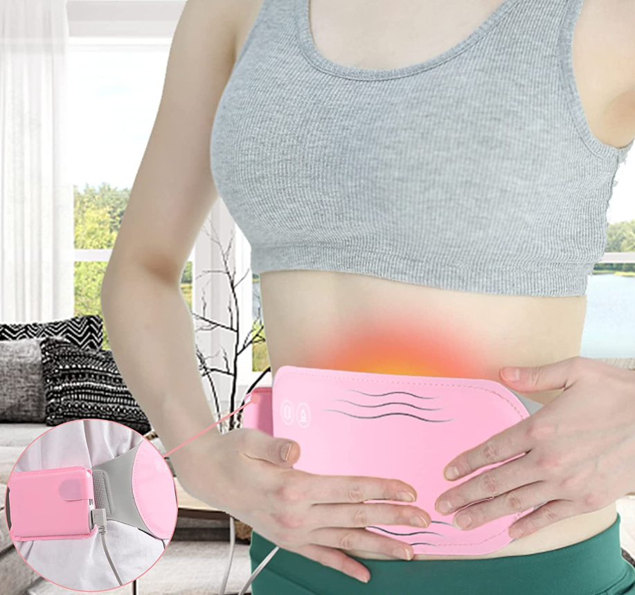 Pink rechargeable belly warmer heating pad under grey crop tank, held on abdomen