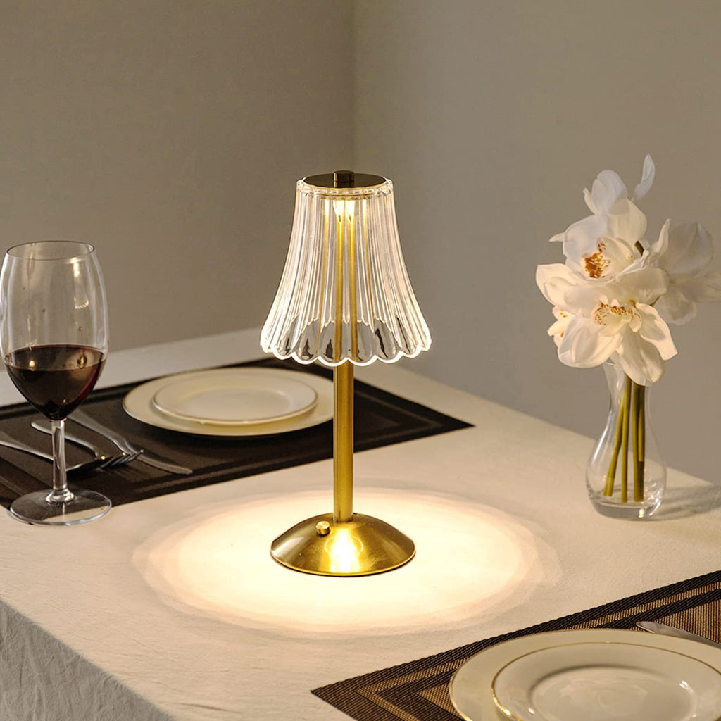 Gold table lamp with clear pleated crystal shade on a round base, warm glow.