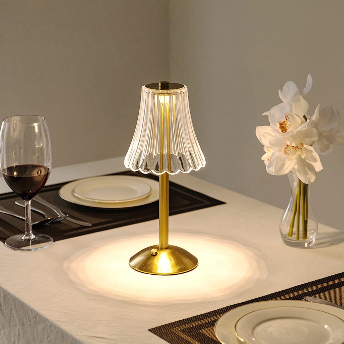Gold table lamp with clear pleated crystal shade on a round base, warm glow.