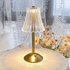 Brushed gold table lamp with clear ribbed crystal shade, illuminated on a fabric table.