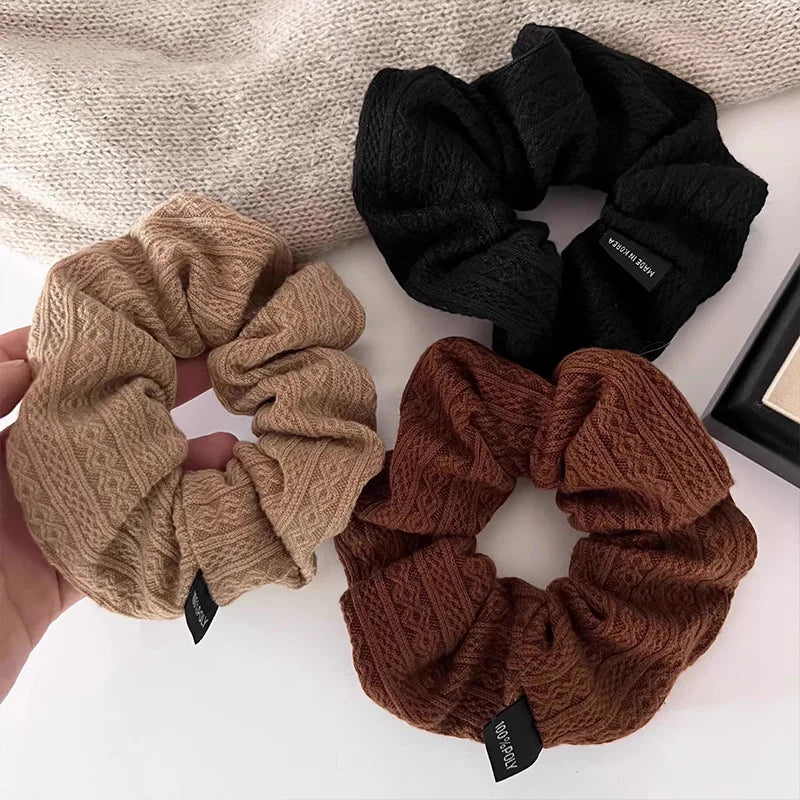 Knit hair scrunchie set in beige, black, rust, and dark brown with textured pattern.