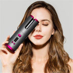 Gray cordless automatic curling iron with pink trim beside a user.