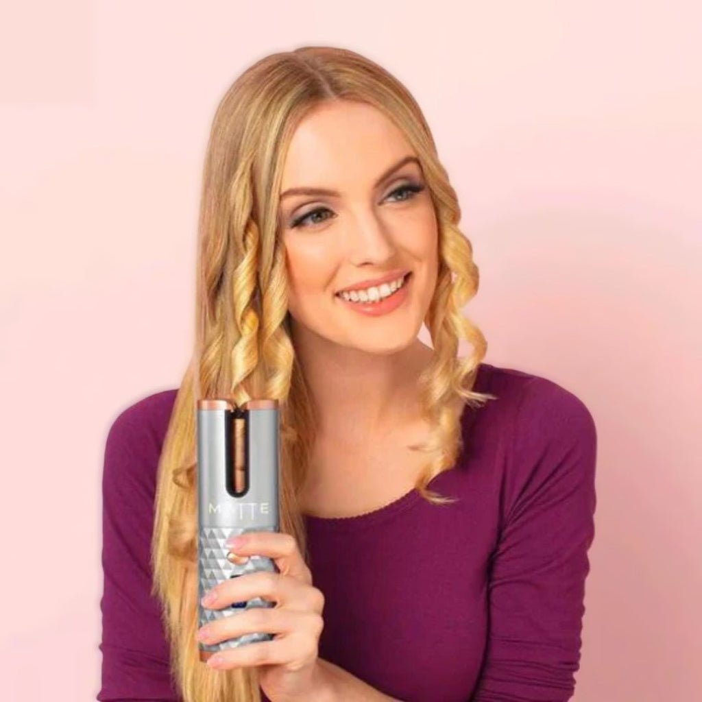 Automatic curling iron in silver tones with pink accents, held in hand.